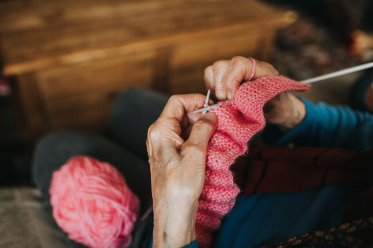 Elderly woman knitting a pink blanket.