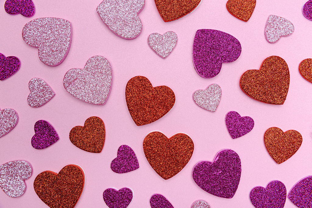 Pink and red glittery hearts in different sizes spread out over a pink background.