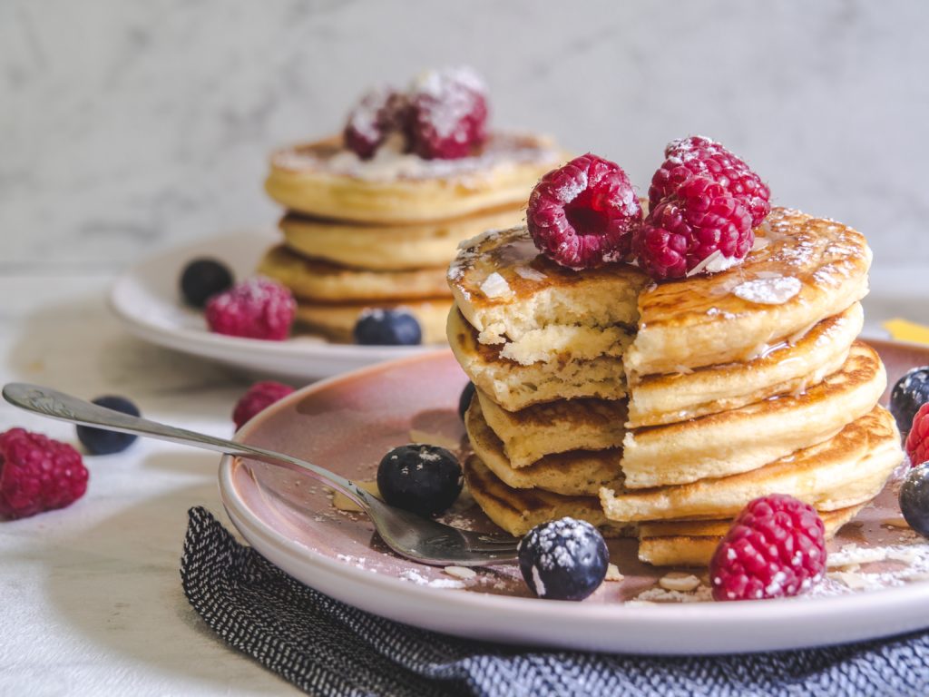 two plates with pancakes in a pile and berries