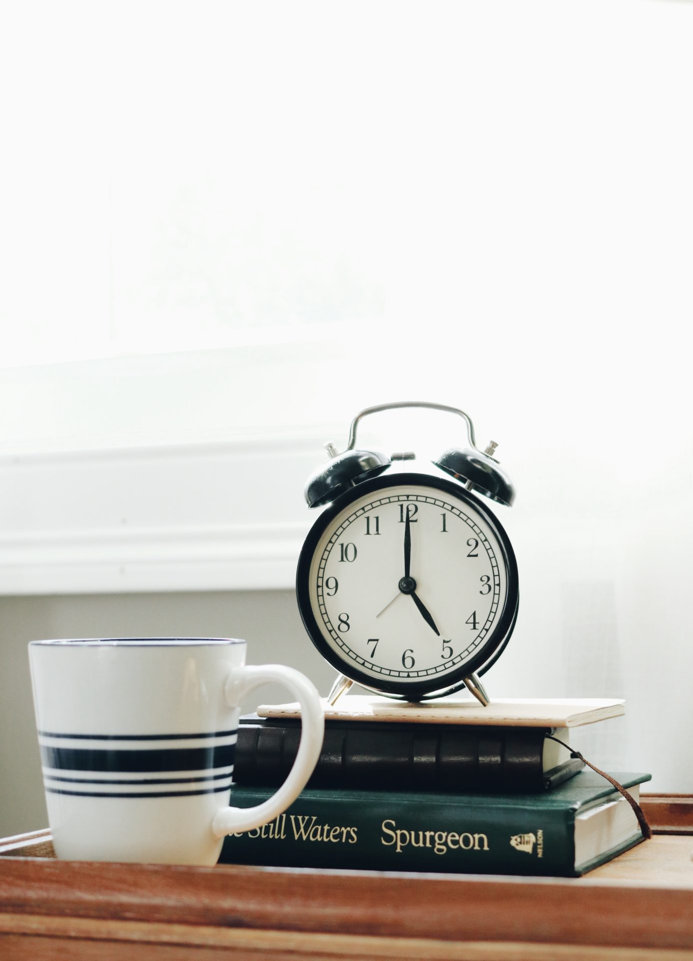 white ceramic mug beside white and black analog alarm clock sat on a pile of books