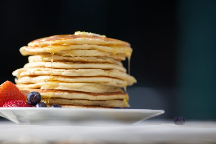 pile of pancakes on a plate drizzled in syrup with strawberries and blueberries to the side