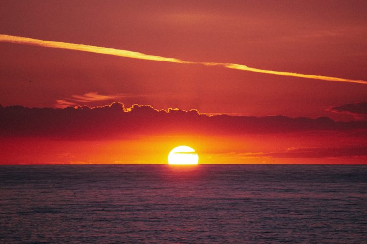 a sunset over the sea making the sky orange with thin layers of cloud