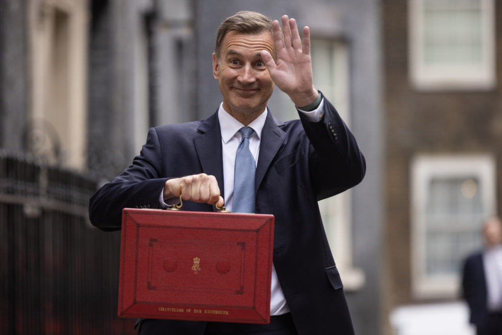 Jeremy Hunt holding red suitcase and waving to camera