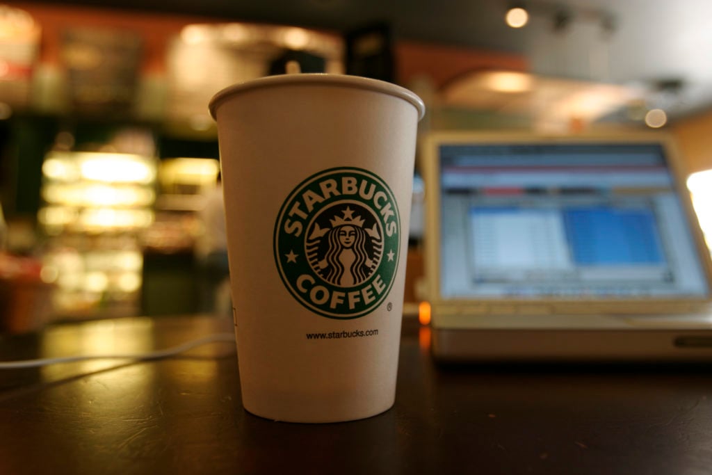 starbucks coffee cup in front of open laptop on table at coffee shop