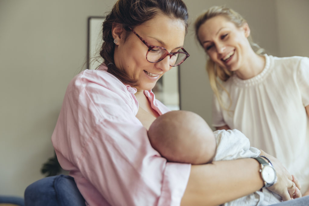 Midwife in white supporting a breastfeeding mother in pink with her newborn baby
