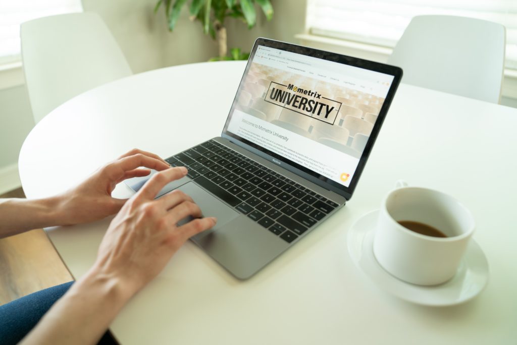 computer screen showing university home screen on a white table next to teacup