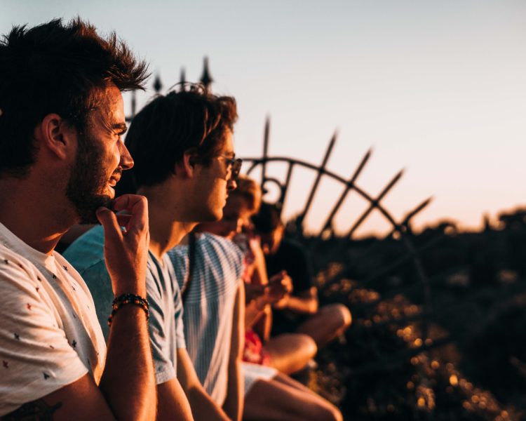 row of men sitting on a wale facing the sunset