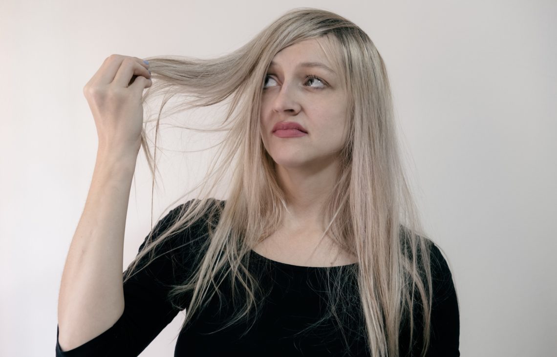 woman in black scoop neck shirt holding up blonde hair looking disappointed