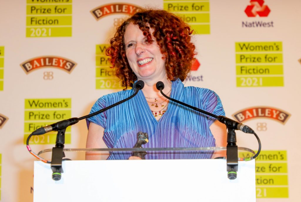 Maggie O'Farrell in blue and purple dress stood behind podium smiling at Women's Prize For Fiction event