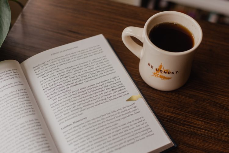 open book next to mug filled with coffee on wooden table