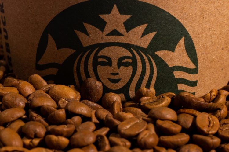 close up of a starbucks cup with lots of coffee beans in front of it.