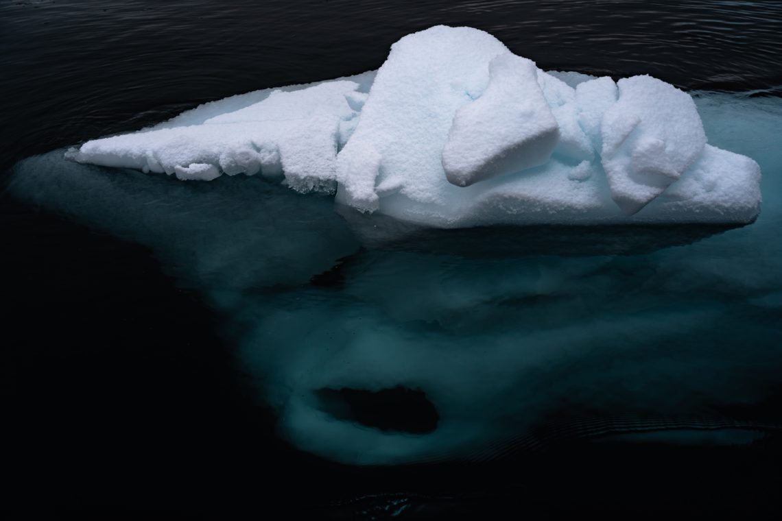 iceberg in dark body of water with some below the surface