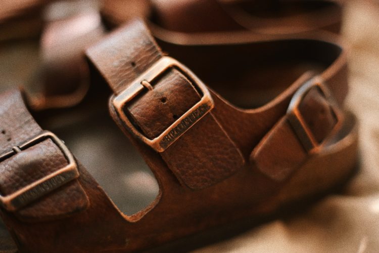 a pair of brown sandals sitting on top of a bed with two buckles