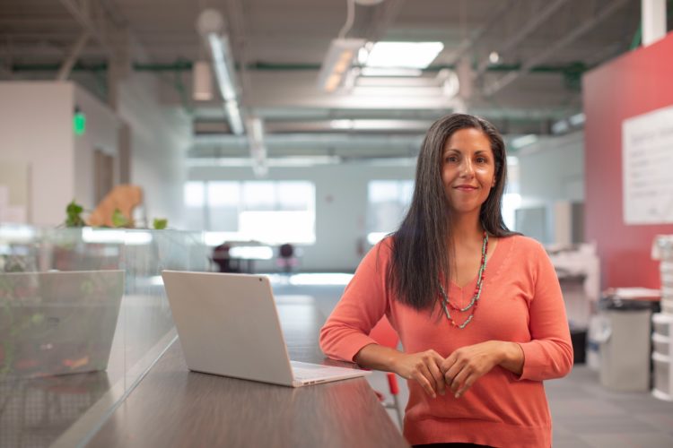 woman in orange long sleeve shirt standing beside table with macbook pro