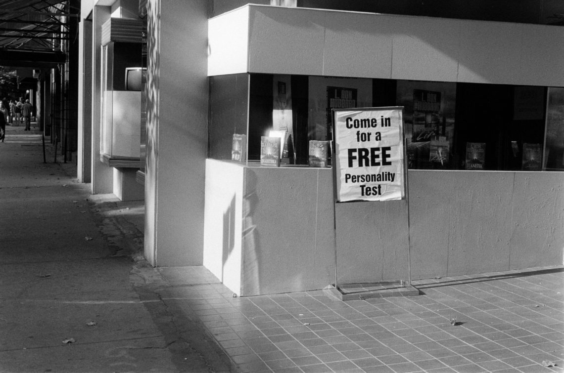 black and white photo of sign advertising personality test leaning against wall
