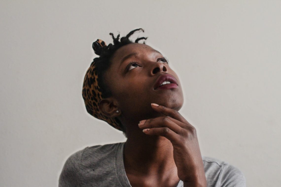 woman in grey top with hand on chin looking up and confused