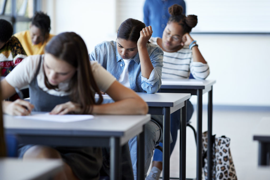 Three female students sat in front of one another taking test in classroom