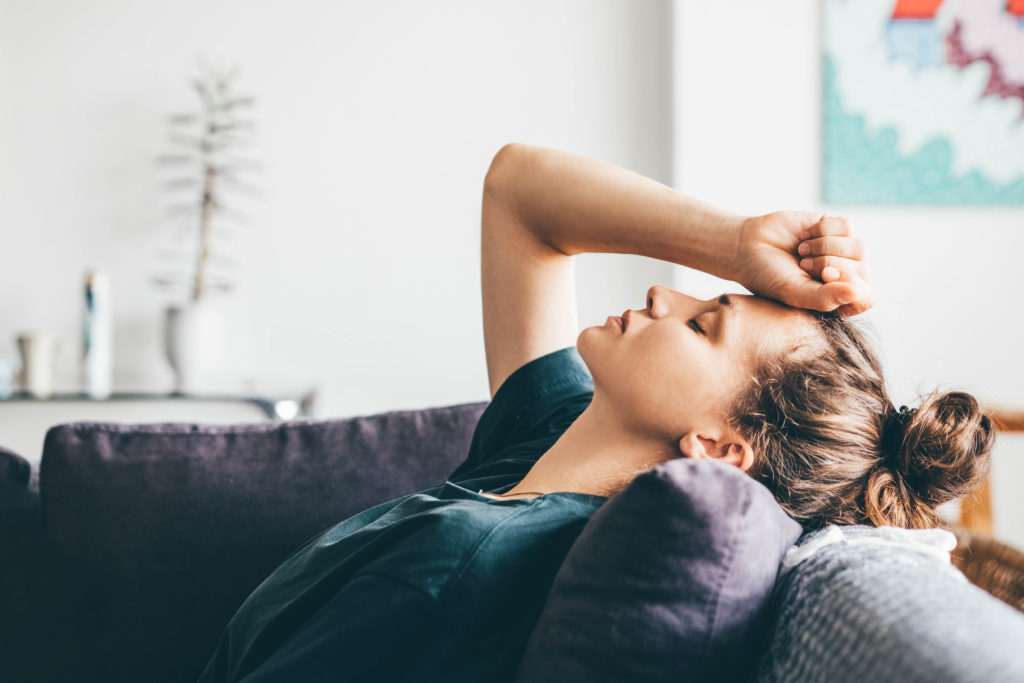 Woman in green top leaning back into sofa with fist resting on forehead looking stressed