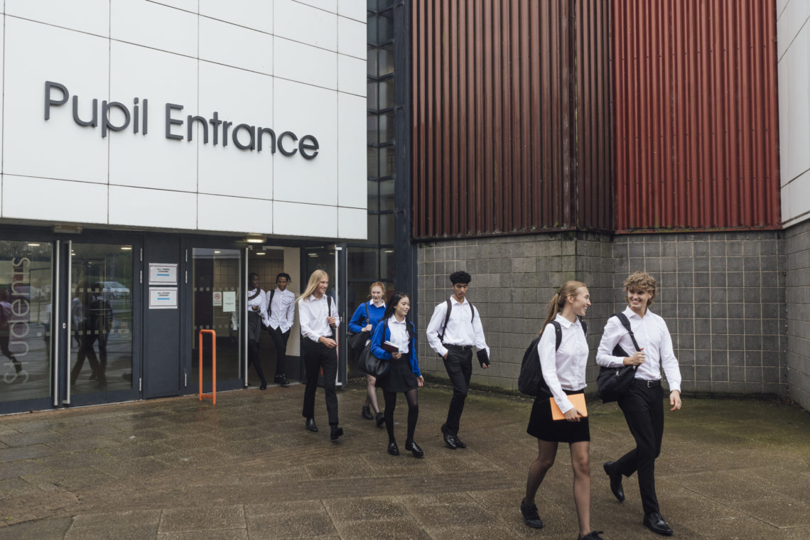 Students wearing school uniform, leaving school for the day in Gateshead, North East England. They are talking to each other while walking out of t...