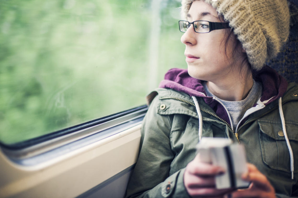 Teenage girl sat on a train holding a train ticket and her phone, looking out of the window.