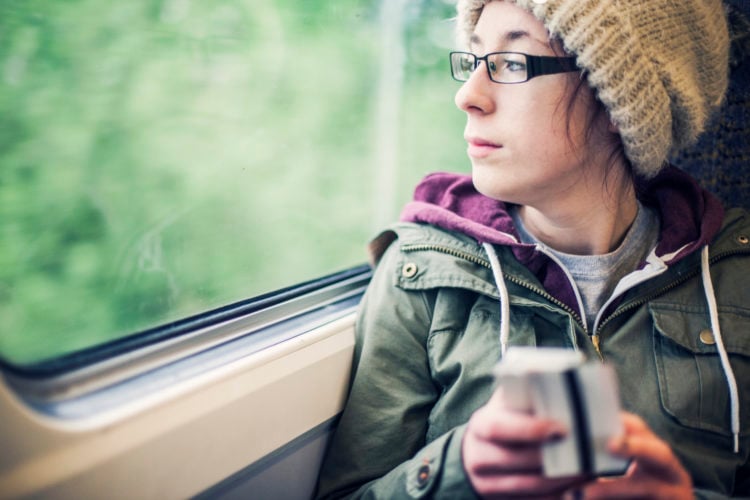 Teenage girl sat on a train holding a train ticket and her phone, looking out of the window.