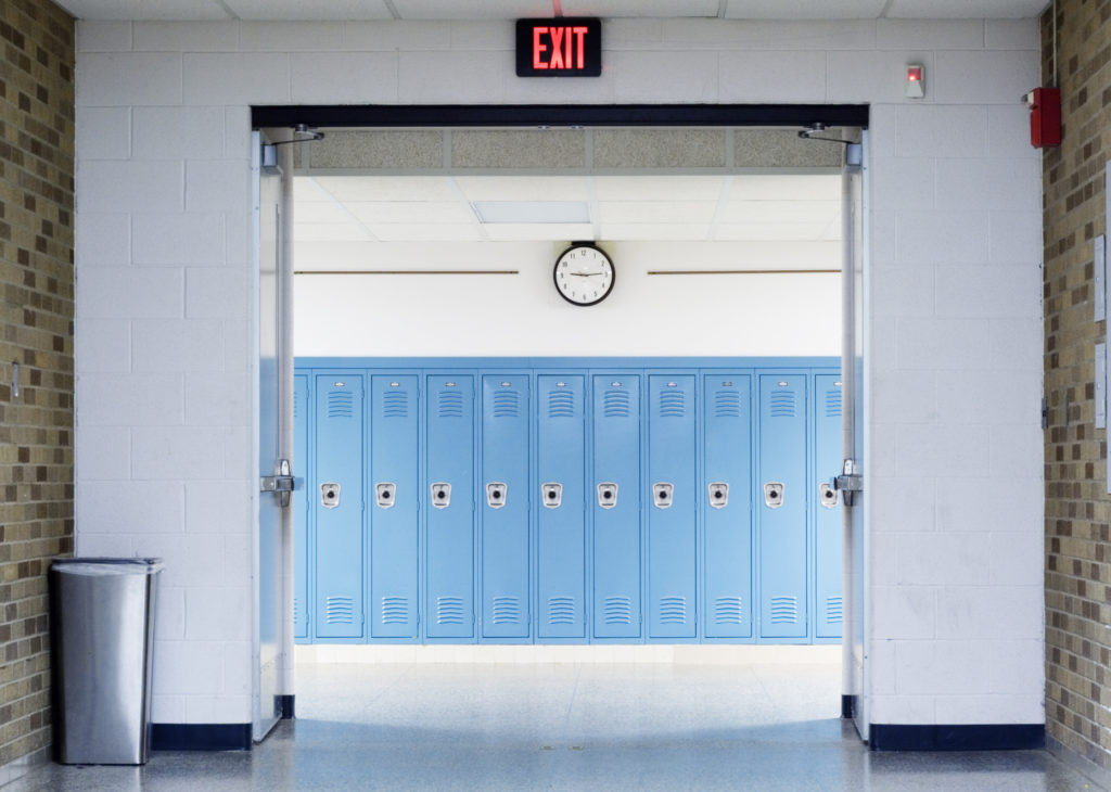 school hallway with red exit sign above doorway with blue lockers on otherside