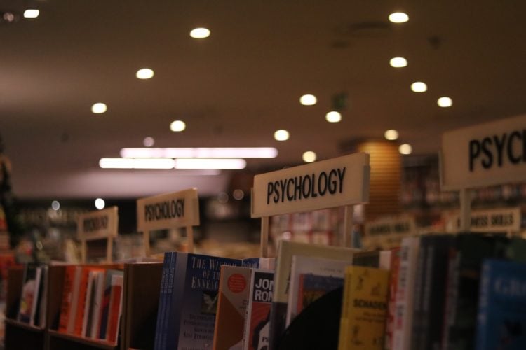 rows of psychology books on shelves in the middle of a dimly lit library