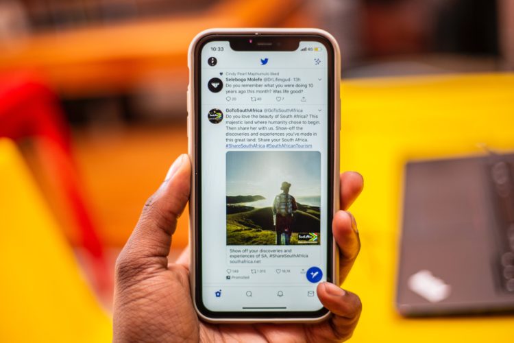 hand holding iphone displaying twitter feed with yellow desks in background