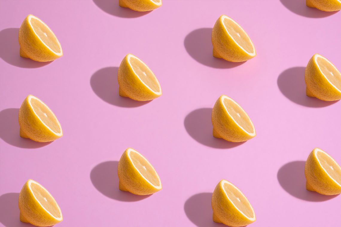 multiple sliced lemons balances facing up casting shadows on pink background