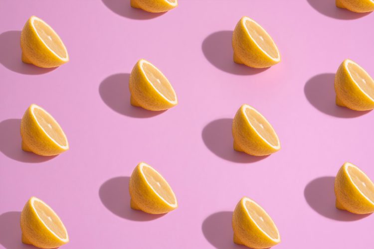 multiple sliced lemons balances facing up casting shadows on pink background