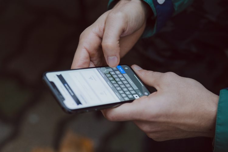 pair of hands holding phone and typing out a message whilst stood outside