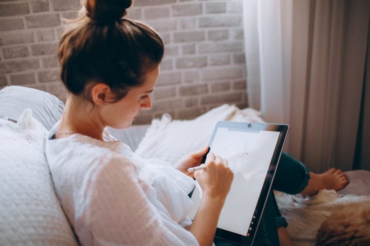 Young woman sat on sofa in white shirt using iPad