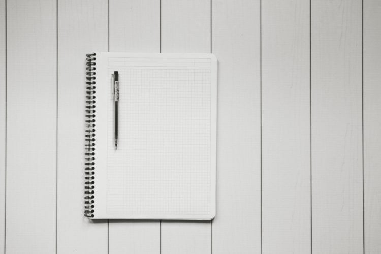 Blank notebook with pen resting on top on white wooden background