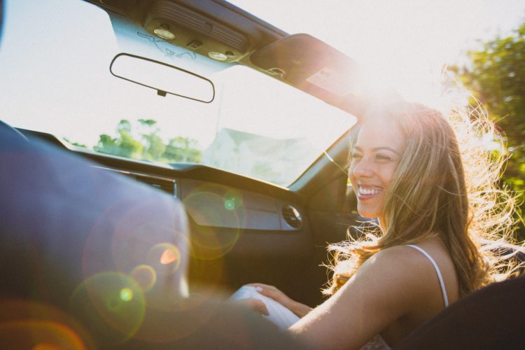 smiling woman sitting as a passenger in a convertible car at daytime