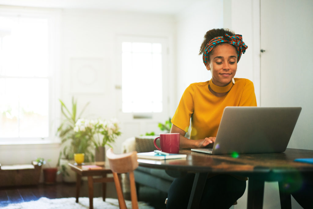 young woman in yellow jumoer sat at table using laptop on bright day