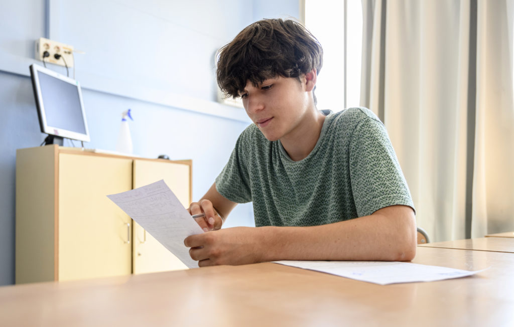 make student in green stop looking at results whilst sat at wooden table