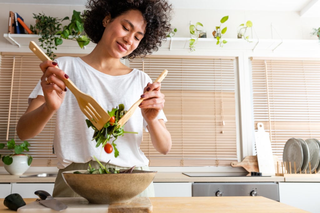 Young woman tossing salad smiling in a kitchen