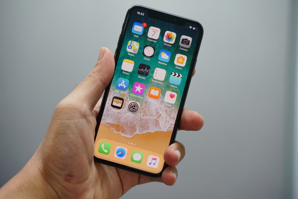 close up of person holding iphone displaying home screen with beach background