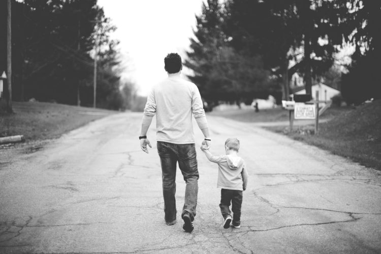 black and white photo from behind of dad holding son's handing walking down road