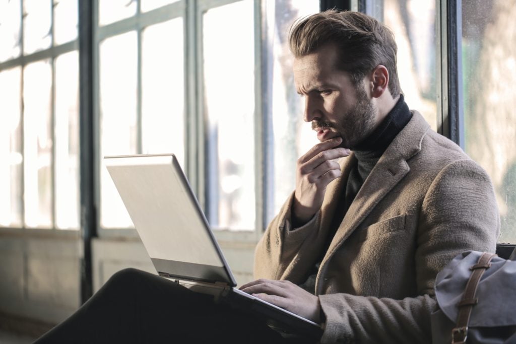 man holding his chin facing laptop computer looking confused