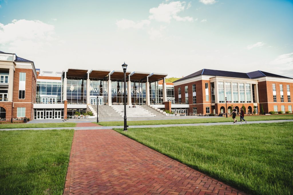 outside of a glass, brown and white university campus building with grass outfront on sunny day