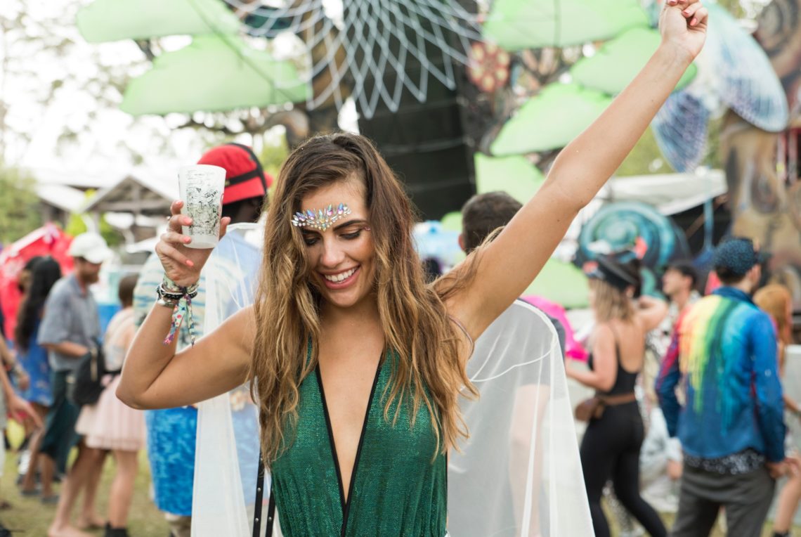 woman in green dress holding up drin and raising hand at a festival