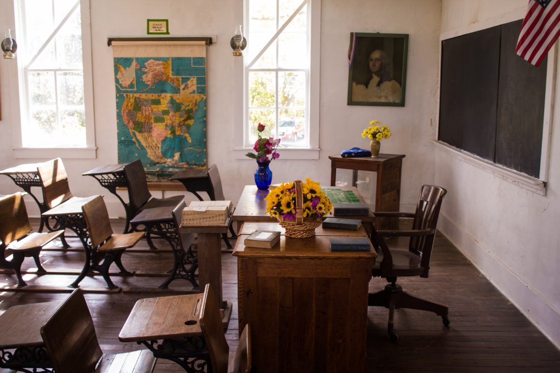 empty classroom with dark wooden table showing teacher's desk near bright windows