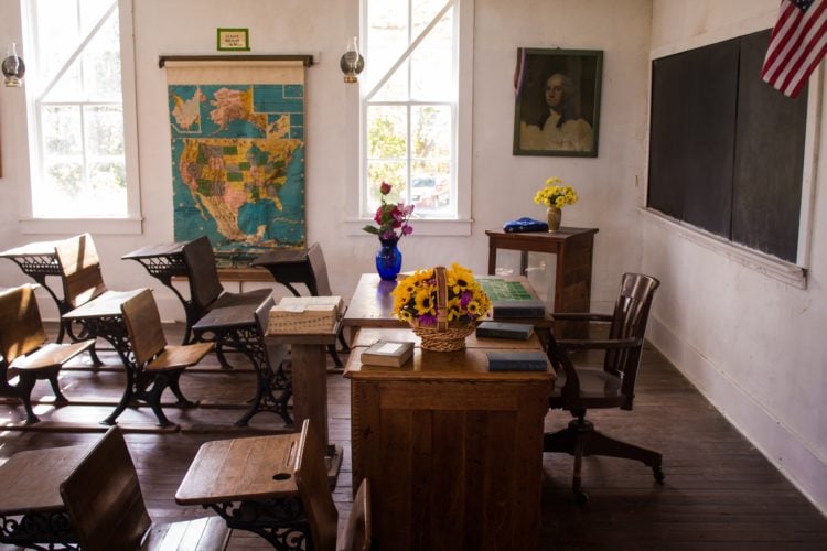 empty classroom with dark wooden table showing teacher's desk near bright windows