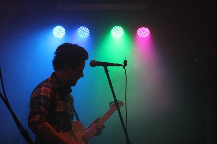 person playing guitar with blue green and pink lighting