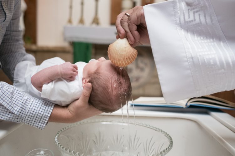 a baby held by mother being baptised with holy waterin a church