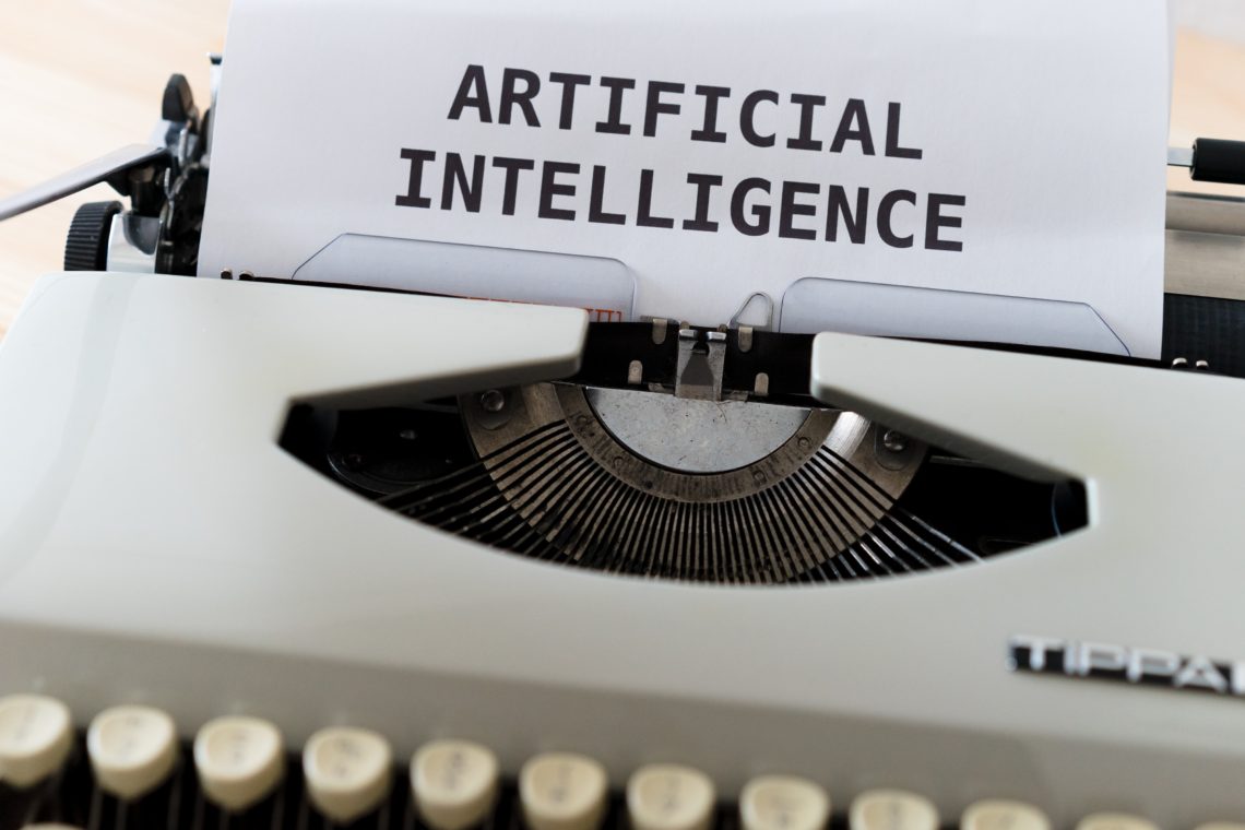 close up of white typewriter with piece of paper with 'artificial intelligence' on