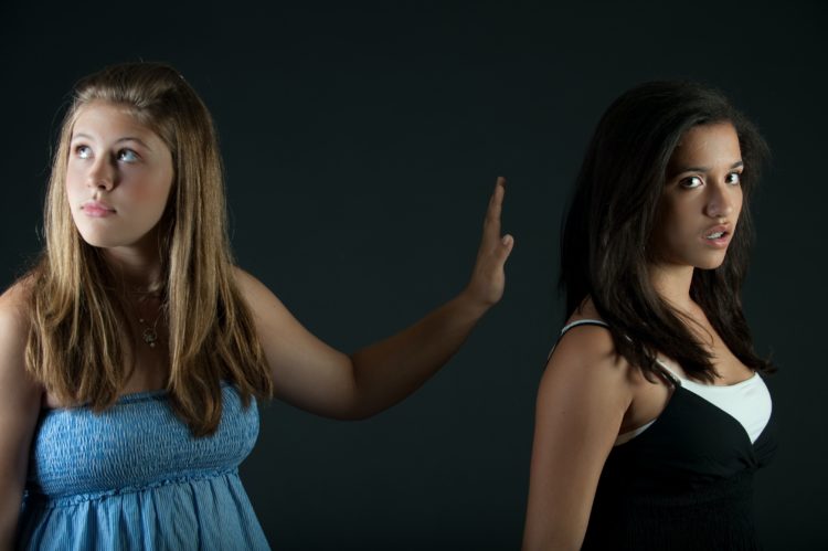 girl in blue sleeveless dress putting hand up and turned away from girl in black and white top