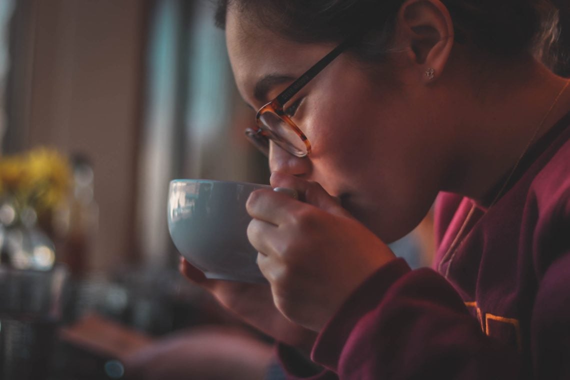 woman drinking tea out of mug wearing a red jumper
