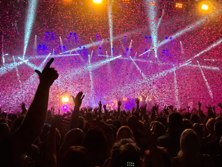 wide shot of a big crowd raising hands at a concert with purple lighting